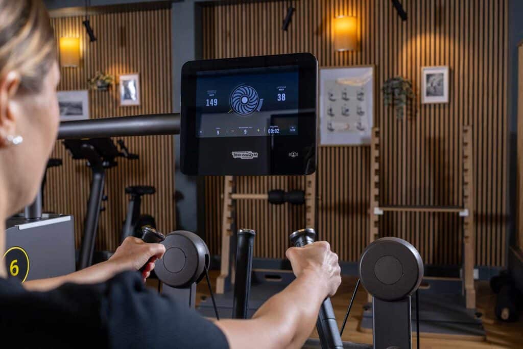 Eine Frau trainiert an einem modernen Fitnessgerät mit digitalem Display von Technogym – Verbindung von Fitness, Physiotherapie und Prävention beim TVG 1893 in Essen, zur Förderung von Gesundheit und Leistungsfähigkeit.